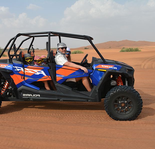 Man and family riding a blue Polaris RZR XP Pro dune buggy rental through Dubai desert with cloudy sky