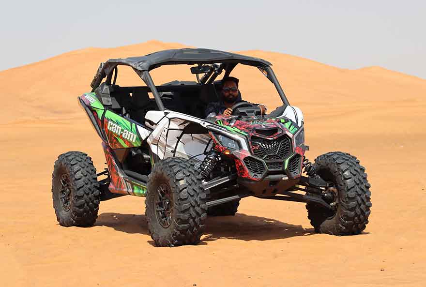 Side View Of A Black And Green Buggy Can-am Riding Through Sand Dunes On A Sunny Day.