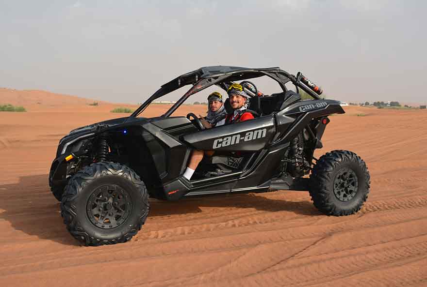 A black Can-Am Desert Dune Buggy Rental Buggy Passing Through A Desert along with 2 people inside.