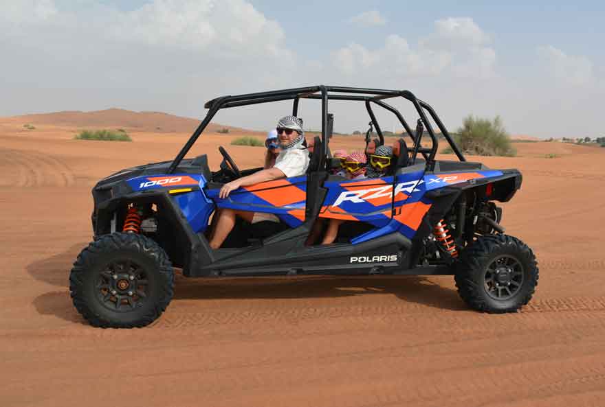 Family riding a blue polaris dune buggy through the Dubai desert .