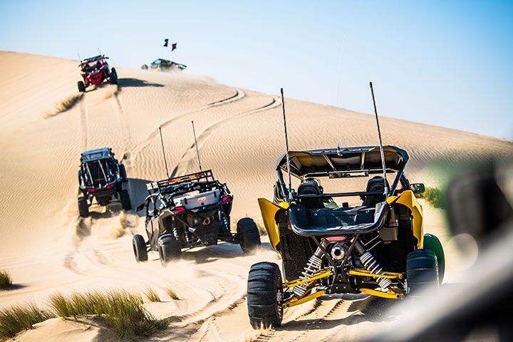 Four off-road Can-Am Buggy Maverick x3 buggies driving on a sandy hill