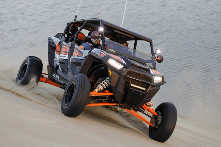 Family riding a thrilling back and orange can-Am Buggy Ride throwing dust behind the trail
