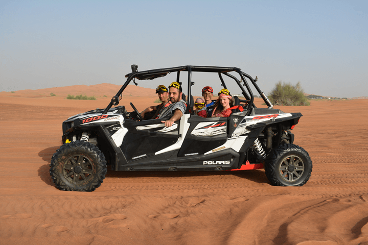 Family riding a black polaris dune buggy through the Dubai desert.