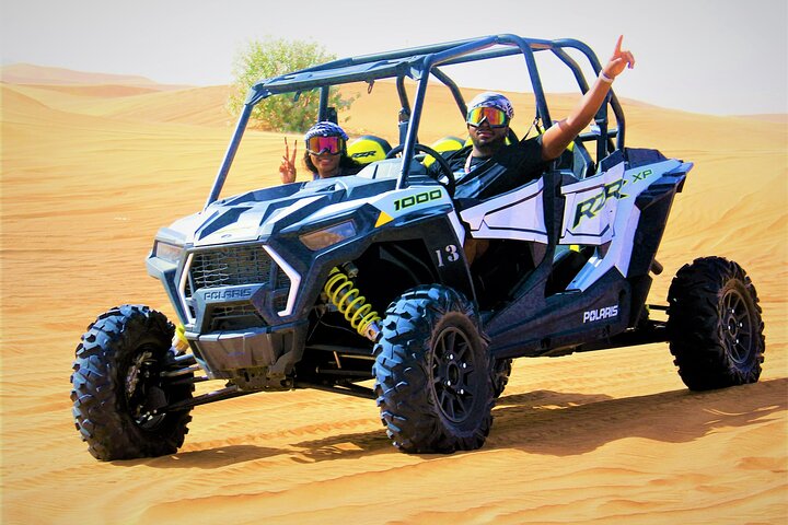 Couple riding A blue Polaris Speeding Through A Desert along with 2 people inside posing for picture.