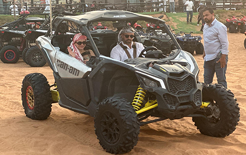 Couple wearing traditional desert headscarves riding a Can-Am Maverick dune buggy at an adventure camp in Dubai.