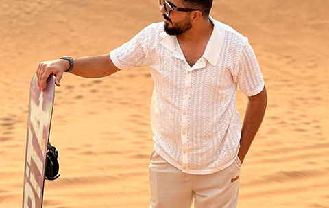 Man standing on a Dubai sand dune holding a sandboard, preparing for a desert sandboarding adventure.