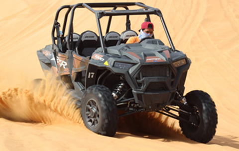 A Red And Black Buggy Driven Super Fast In The Desert Leaving Sand Behind.
